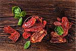 Delicious dried tomatoes with fresh basil herbs on brown wooden vintage textured background, top view. Traditional mediterranean kitchen.