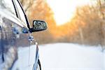 Close up Image of Side Rear-view Mirror on a Blue Car in the Winter Landscape with Evening Sun