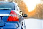 Blue Car on the Winter Snowy Road at Sunset. Close up Rear View. Travel and Safe Driving Concept.