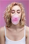 studio closeup portrait of blond woman with curly hair doing a bubble with a chewing gum on a pink background