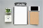 Table top view of office desk with notebook mobile phone and stationery items on grey background