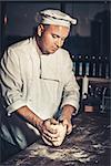 Italian chef in hotel or restaurant kitchen knead the dough on the table. Pizza cooking