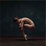 young beautiful ballet dancer in beige swimsuit posing on pointes over dark grunge background