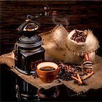 Cup of coffee, cinnamon sticks, star anise, a bag of roasted coffee beans on sackcloth stand on a glossy black surface, on a brown background
