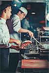 Busy chefs at work cooking beef steak in the interior of modern professional kitchen