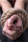 Tied thick rope hands of woman hostage on blank background