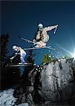 Skiers jumping over rock