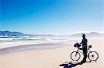 Black man with bike standing on beach