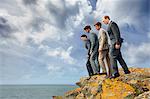 Businessmen peering over cliff edge