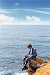 Businessman using laptop on cliff