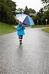 Toddler boy carrying umbrella on road