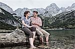 Smiling couple dangling feet in lake