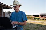 Farmer using laptop by barn