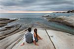Couple relaxing on boulder by ocean