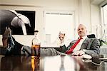 Senior businessman with feet up on desk drinking spirits