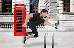Hurdler jumping hurdle with red telephone box in background