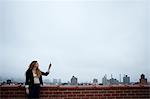 Businesswoman on rooftop holding up cell phone to find signal