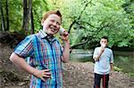 Two boys using paper cups and string to communicate in woodland