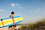 Teenager carrying surfboards to beach beside dunes