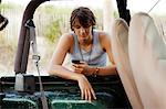 Teenager leaning against jeep checking phone