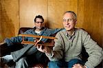 Father holding toy plane with adult son on couch, smiling