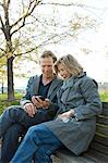 Mother and adult son on park bench looking at smartphone