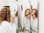 Young woman applying make-up in mirror