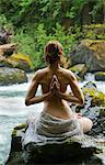 Rear view of topless woman meditating on rock by water