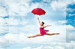 Ballerina with umbrella, leaping against cloudy sky