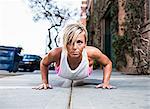 Young woman doing push-up on city street