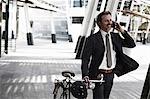 Mid adult businessman walking with bicycle and using mobile phone