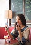 Mid adult women using mobile phone to apply lipstick in restaurant
