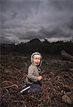 Young boy kneeling on ground crying against stormy sky