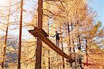 Mature woman climbing in forest, attached to high line rope