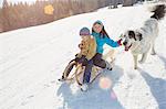 Brother and sister tobogganing with pet dog