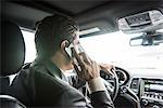 Over the shoulder view of young businessman driving whilst talking on smartphone