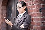 Businesswoman using smartphone next to brick wall
