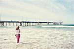 Rear view of woman paddling in front of pier, Venice Beach, Los Angeles, California