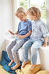 Two young brothers, sitting in window seat, looking at digital tablet