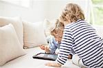 Two boys sitting on sofa using digital tablet