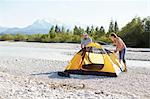 Couple erecting yellow tent near water, Wallgau, Bavaria, Germany