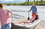 Couple carrying dinghy to water holding paddle