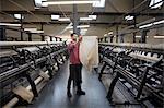 Portrait of male weaver examining cloth from old weaving machine in textile mill