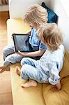 Two young boys, sitting on sofa, looking at digital tablet