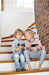 Two young boys, sitting on stairs, looking at smartphones