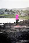 Woman at coast practicing yoga with arms raised, Hawea Point, Maui, Hawaii, USA