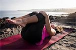 Woman at coast practicing yoga lying on back, Hawea Point, Maui, Hawaii, USA