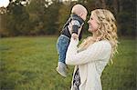 Mid adult woman holding up baby son in field