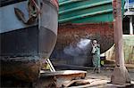 Shipyard worker cleaning boat hull with high pressure hose