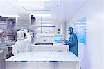 Workers using manufacturing machinery in flexible electronics factory clean room
